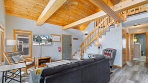 Un vaste espace de vie doté d’un plafond en bois, d’un canapé, d’une télévision, d’une cheminée et d’un escalier.
