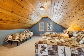 A cozy attic bedroom with wooden slats on the ceiling, two windows, and a bed with a quilt.