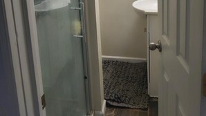 Casa de banho com divisória de chuveiro em vidro, uma pequena janela e lavatório.