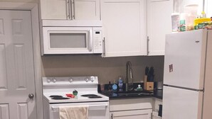 Cozinha compacta com micro-ondas, fogão, forno, frigorífico e uma pequena mesa com um comando remoto.