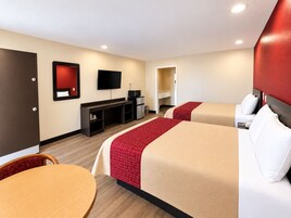 Habitación de hotel con dos camas, un escritorio, un televisor y una puerta.