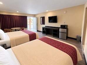 Habitación de hotel con dos camas, un escritorio, un televisor y una kitchenette pequeña.