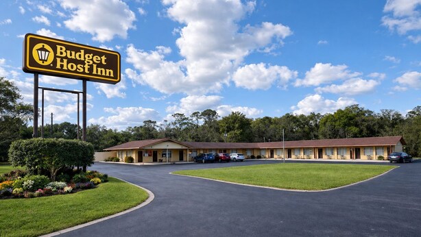 Een Budget Host Inn met een parkeerplaats, een gazon en een rij motelkamers.