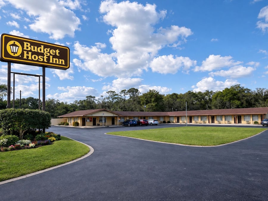A Budget Host Inn with a parking lot, a lawn, and a row of motel rooms.