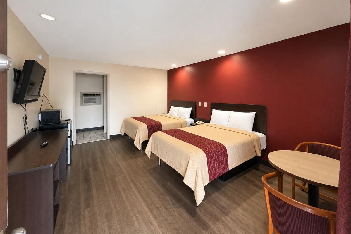 Habitación de hotel con dos camas, un escritorio, una silla y un televisor.