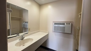 Une salle de bain avec un lavabo blanc, un miroir et un climatiseur fixé au mur.
