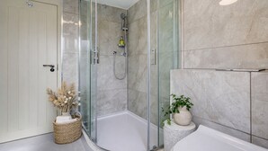 Un baño moderno con ducha envuelta en vidrio, una bañera blanca y pared revestida de mármol.
