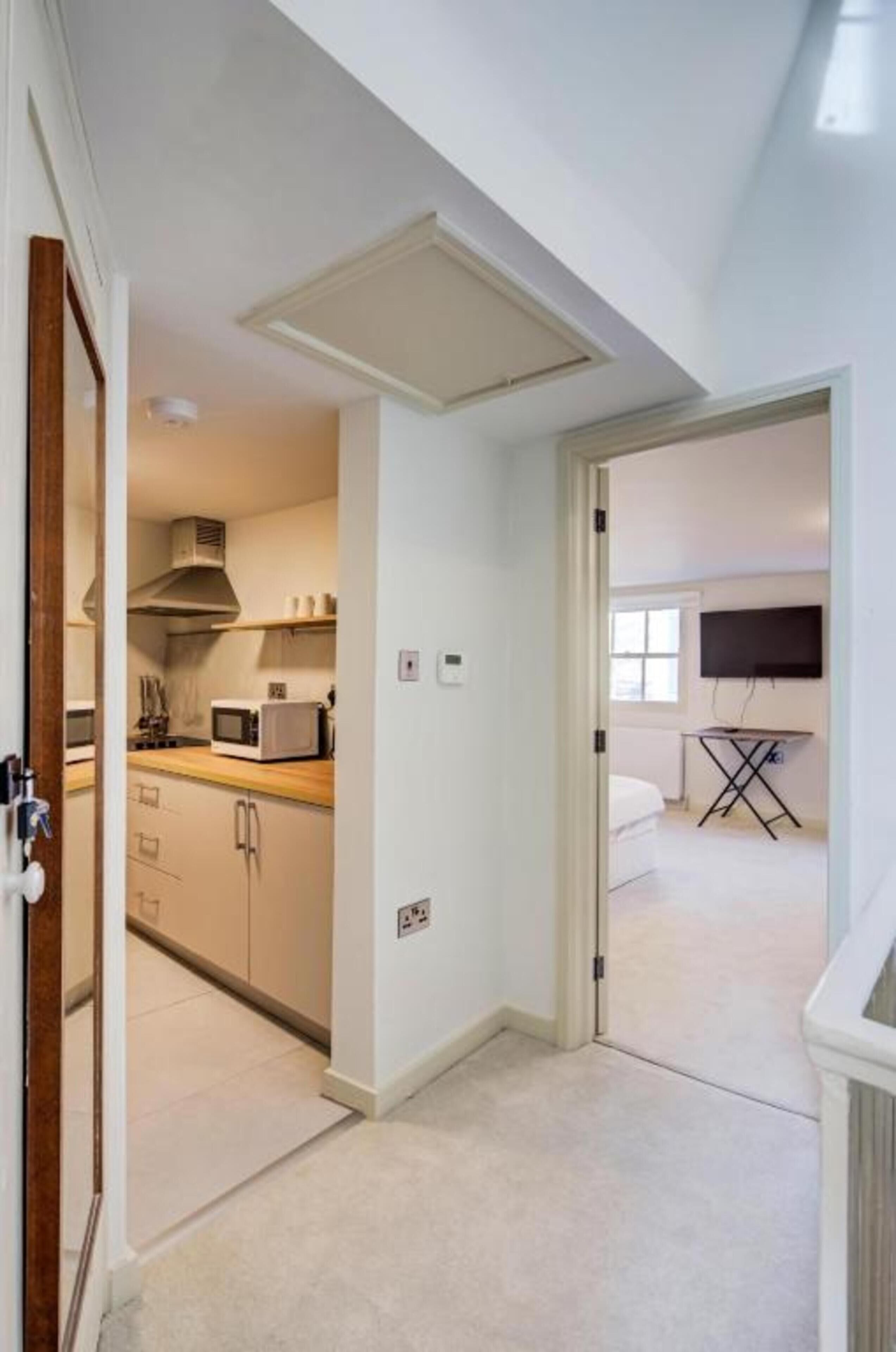 A room with a kitchenette, a flat-screen TV, and a ceiling fan.