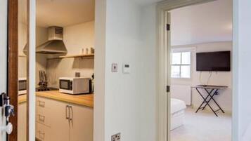 A room with a kitchenette, a flat-screen TV, and a ceiling fan.