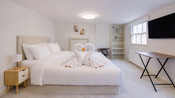 Un dormitorio con cama, mesita de noche, escritorio, estantería y televisor.
