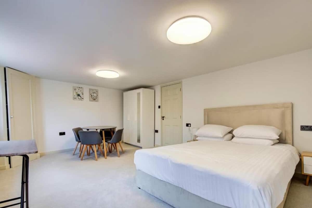A bedroom with a bed, a desk, chairs, and a door.