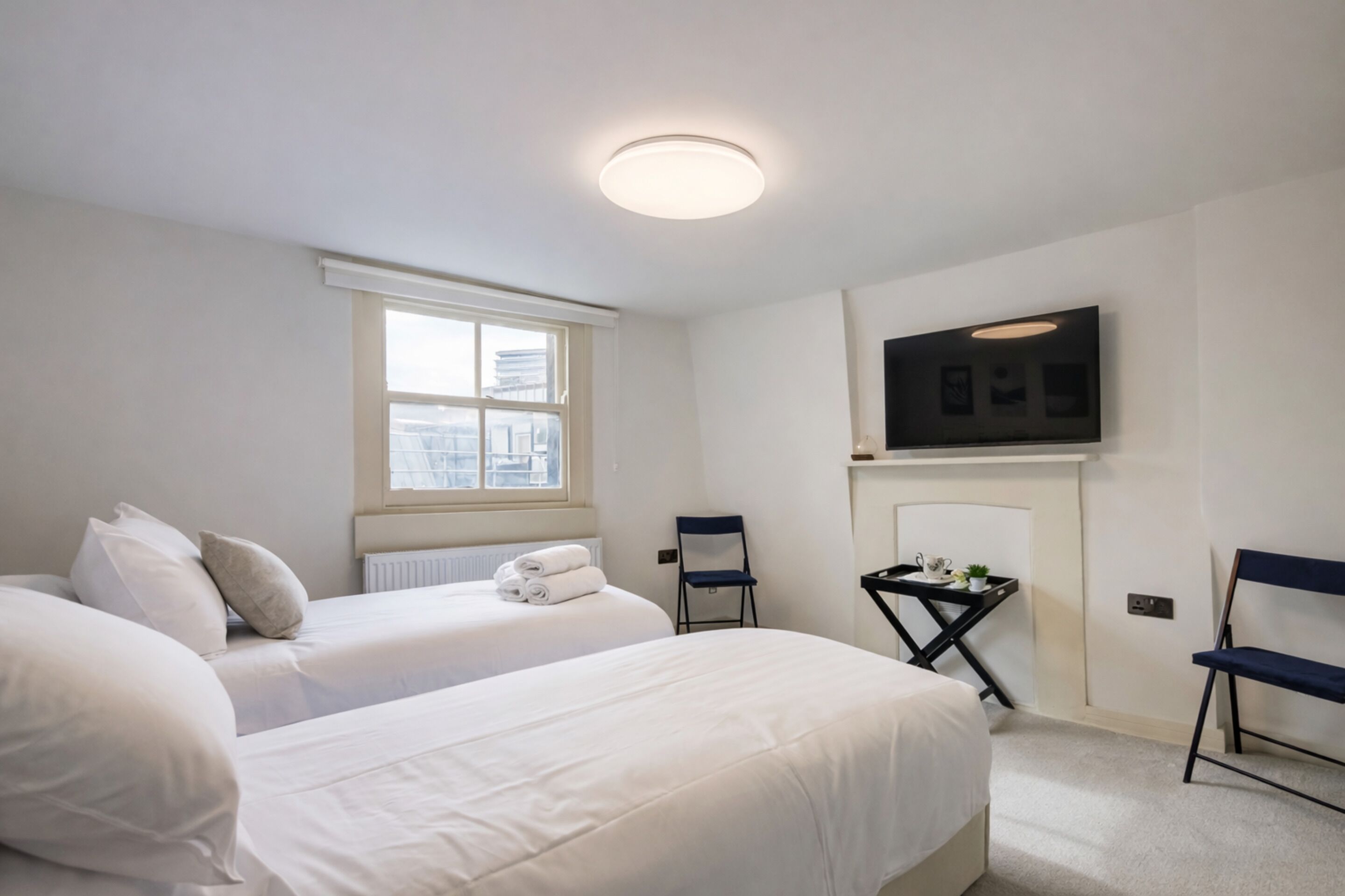 A hotel room with two beds, a TV, a chair, a small table, and a window with a view.