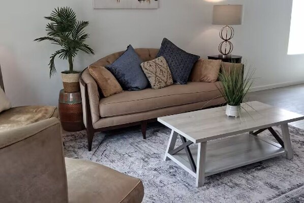 A living room with a sofa, a coffee table, a lamp, and a potted plant. - Brand New Built Modern Oasis-8 Minutes from IAH Airport and restaurants/stores. (Humble)