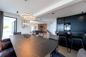 A modern dining area with a large table, multiple chairs, and pendant lighting.