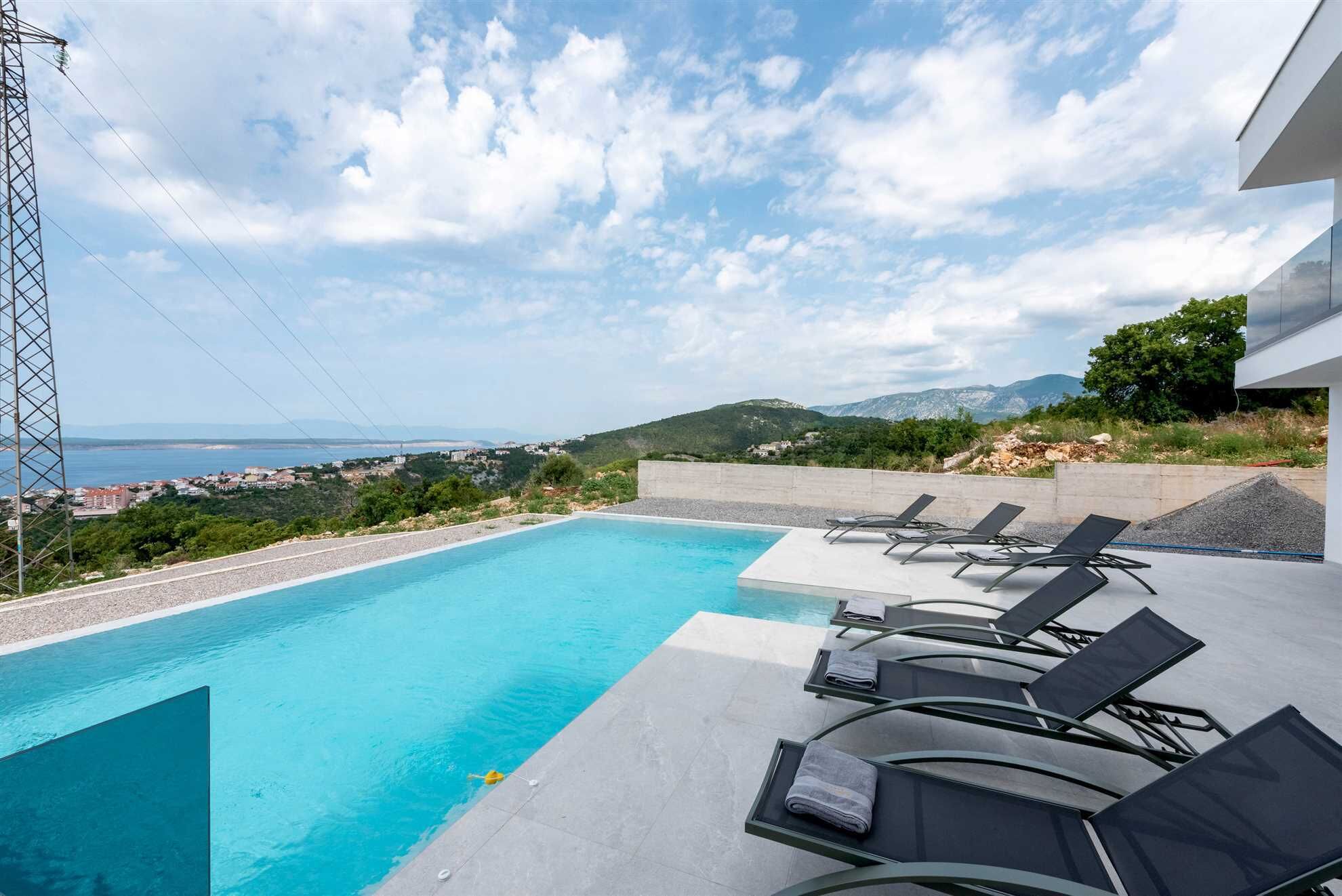 A swimming pool with lounge chairs and a view of a coastal landscape.