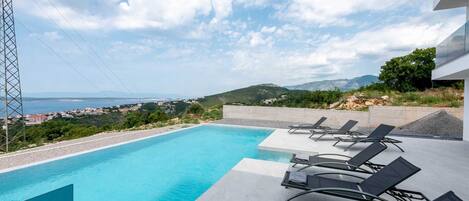A swimming pool with lounge chairs and a view of a coastal landscape.