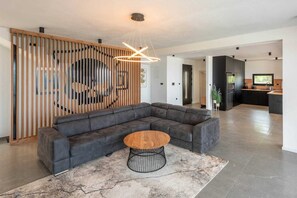 A modern living room with a sectional sofa, a round wooden coffee table, and a contemporary light fixture.