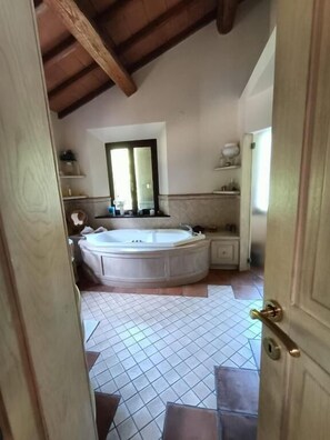 Un baño con una bañera grande, una ventana y piso de baldosas.