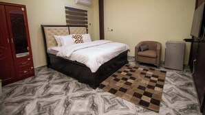 A bedroom with a bed, a chair, a television, and a refrigerator. - NimbusNiche Luxury Residence (Akaikrom)