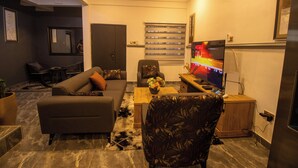 A modern living room with a sofa, a patterned armchair, a coffee table, and a television. - NimbusNiche Luxury Residence (Akaikrom)