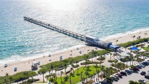 A pier extending into the ocean with a beach and parking area in the foreground. - Bright Studio | Walk to Downtown Lake Worth (Lake Worth Beach)