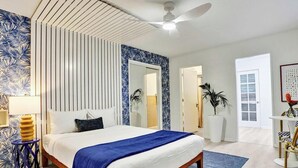 Ein Schlafzimmer mit Bett, Deckenventilator, Spiegel, Tür und Pflanze.