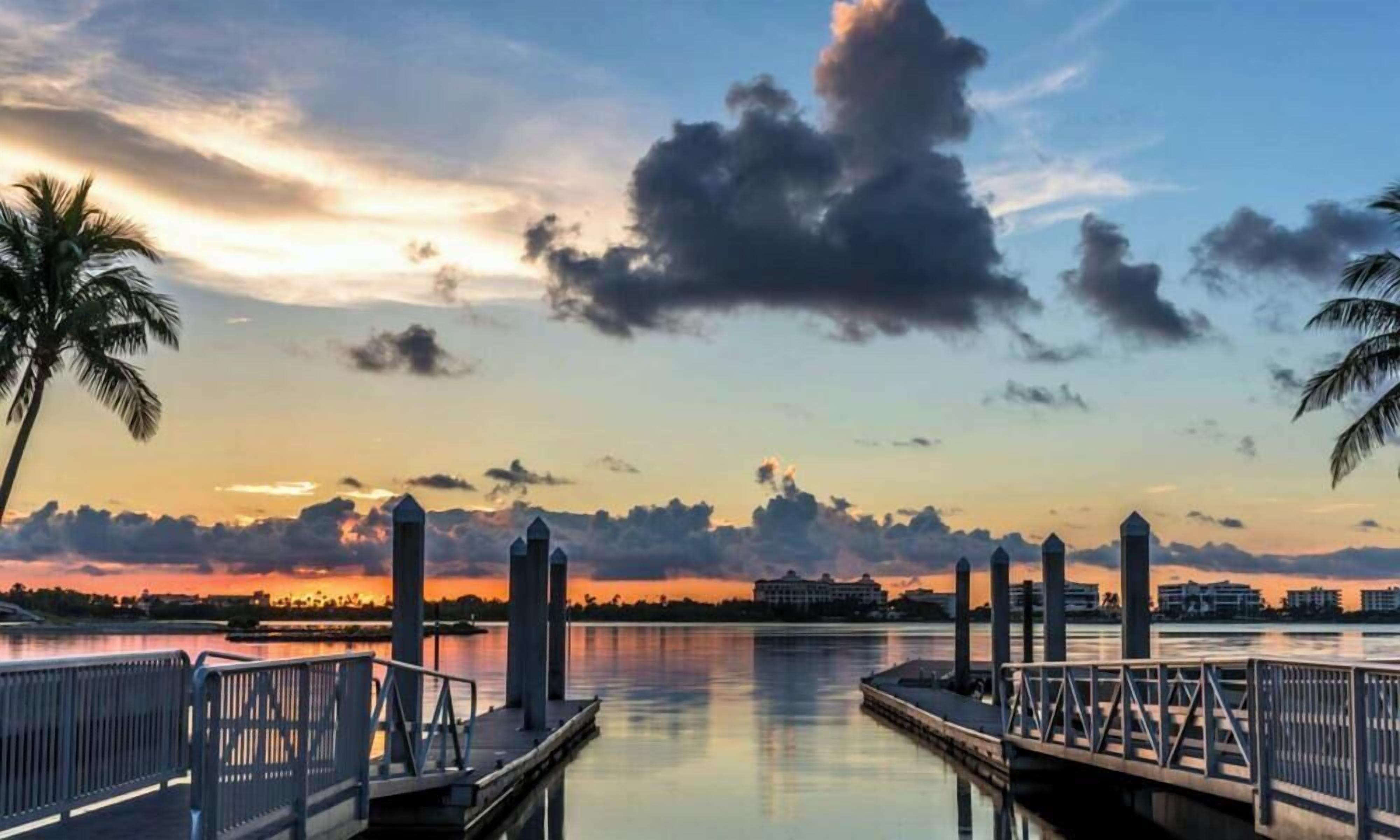 Blick auf das Wasser mit einer Anlegestelle, Palmen und einem Sonnenuntergang.