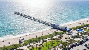 A pier extending into the ocean with a beach and parking area in the foreground. - Downtown Studio | Walk to Lake Worth Beach (Lake Worth Beach)