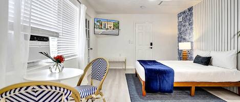 A modern hotel room with a bed, a desk, a chair, a radiator, and a wall-mounted TV.