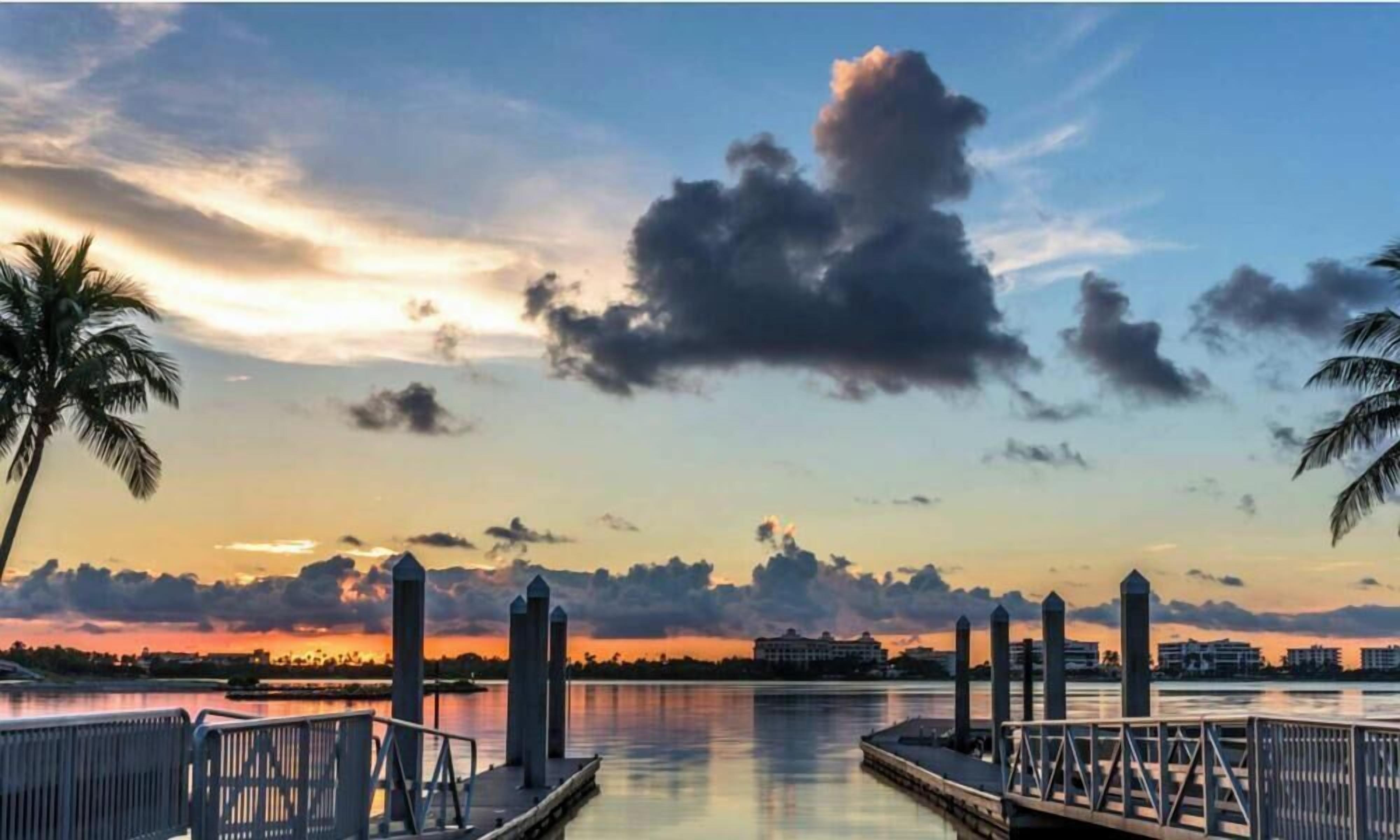 Blick auf das Wasser mit einer Anlegestelle, Palmen und einem Sonnenuntergang.