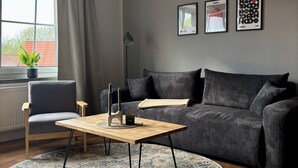 Ett modernt vardagsrum med en soffa, ett soffbord i trä, en fåtölj, en mönstrad matta och ett fönster med gardiner.