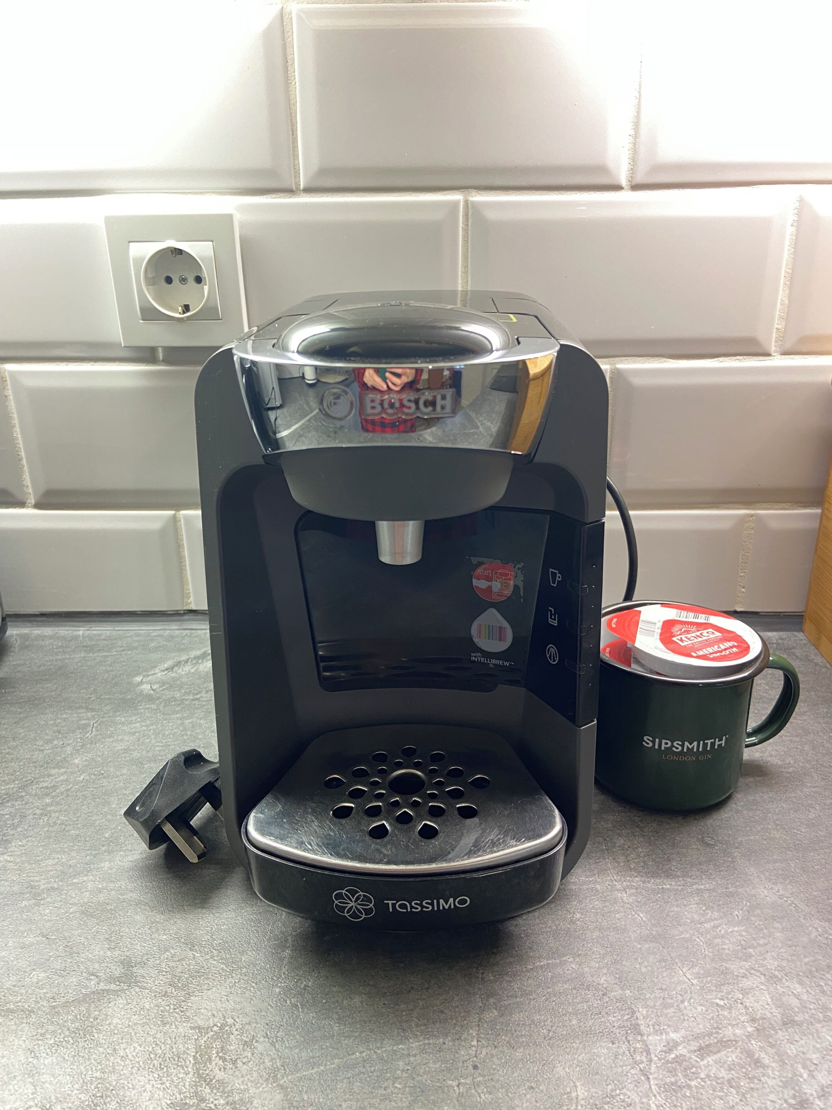 Une machine à café ornée du logo TASSIMO, une tasse verte avec une étiquette rouge et la marque Bosch visible sur l’appareil.