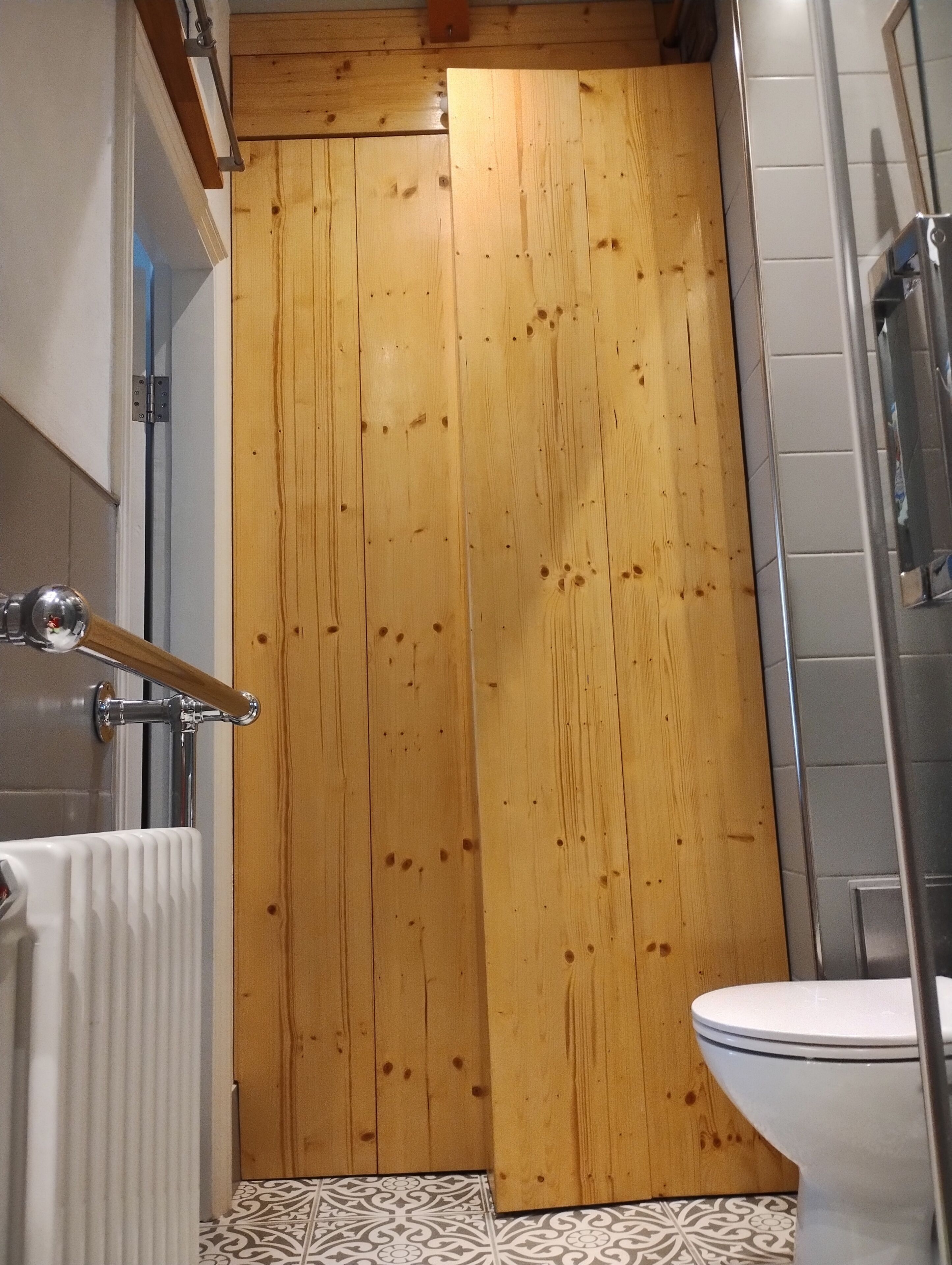 A wooden door in a bathroom with a white radiator and a white toilet.