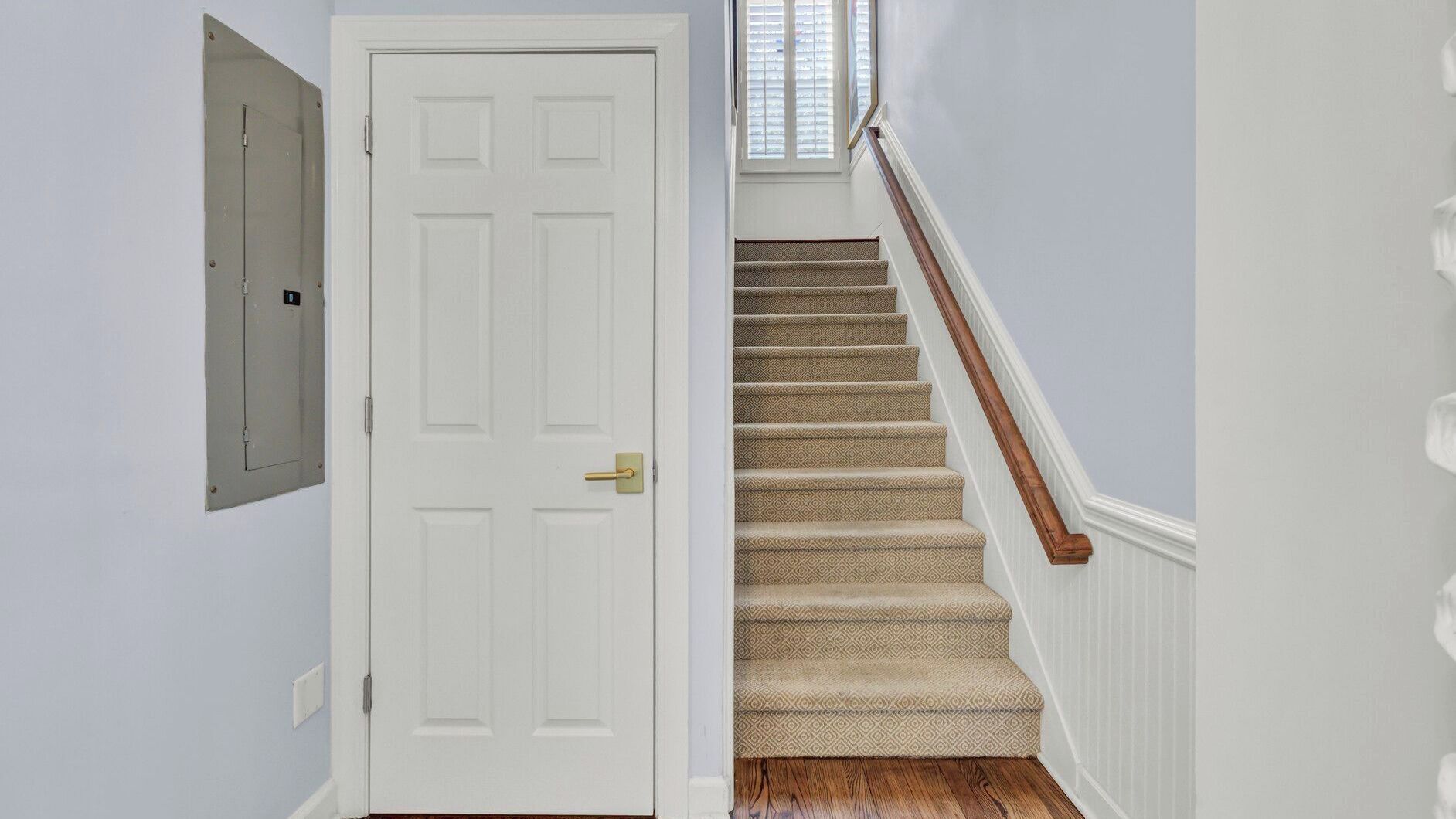 A staircase with carpeted steps and a wooden handrail, leading to a white door with a brass doorknob.