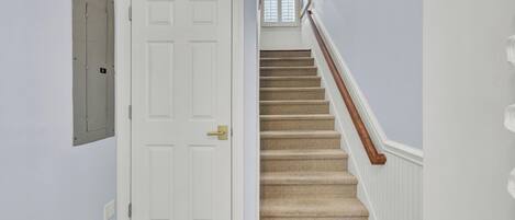 A staircase with carpeted steps and a wooden handrail, leading to a white door with a brass doorknob.