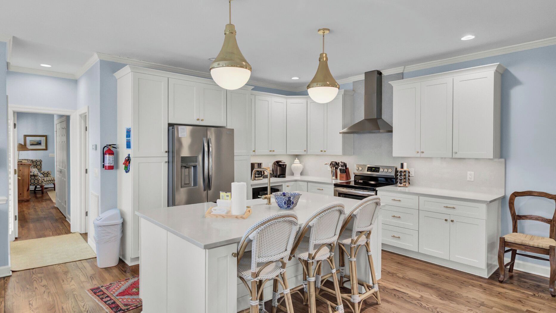A modern kitchen with white cabinetry, stainless steel appliances, and a central island with wicker chairs.