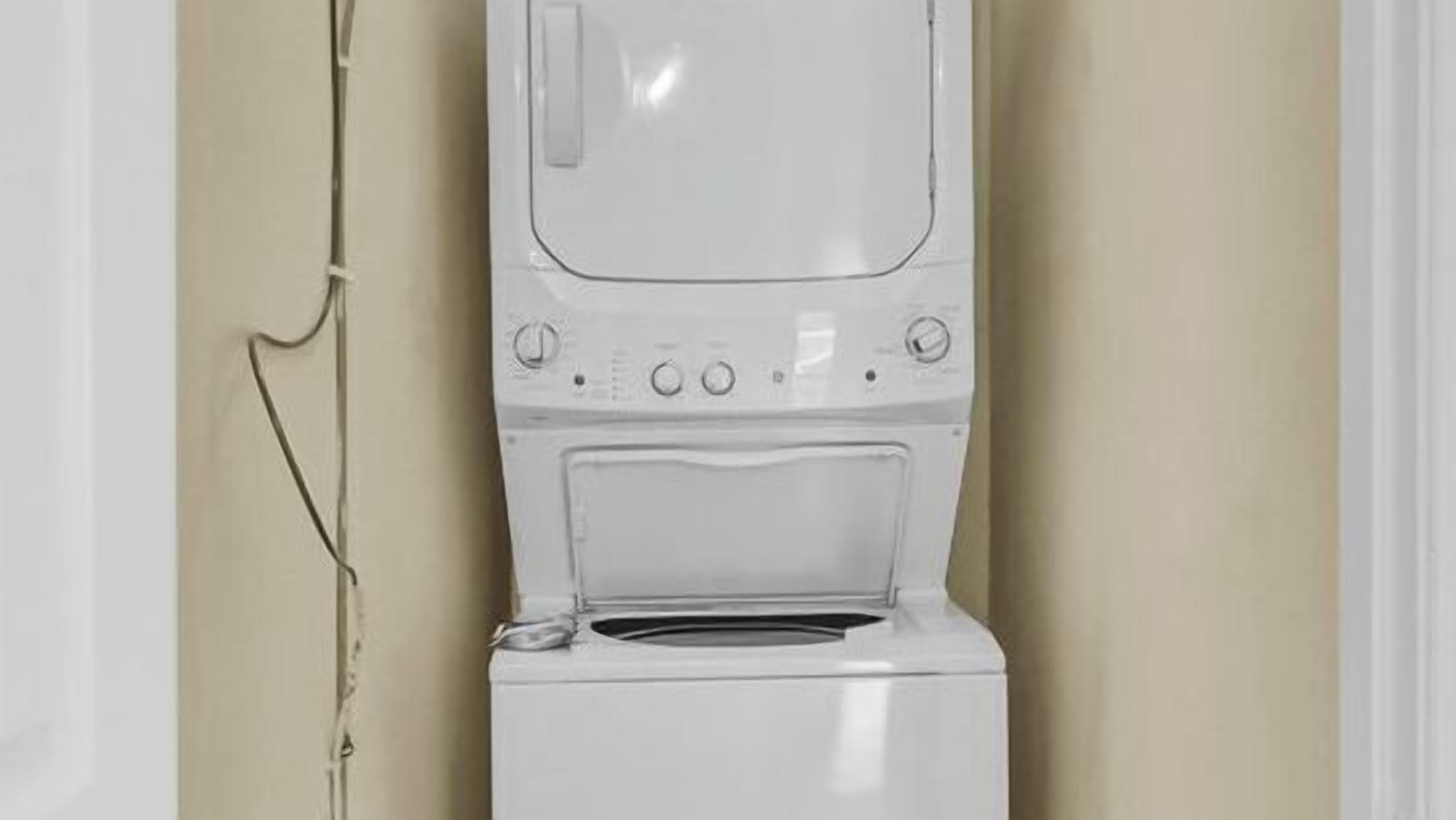 Une vue de face d’un lave-linge blanc, avec ses boutons de commande et sa porte, fixé au mur.