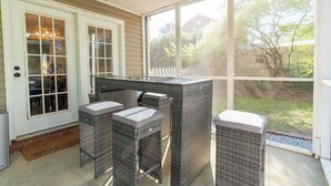 Un portico riparato con mobili in vimini, una porta con pannelli di vetro e vista sul giardino.