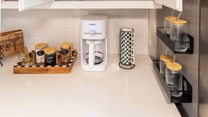 Una cucina con mobili a giorno che espongono bicchieri da vino e tazze, una macchina da caffè e barattoli sul piano di lavoro.