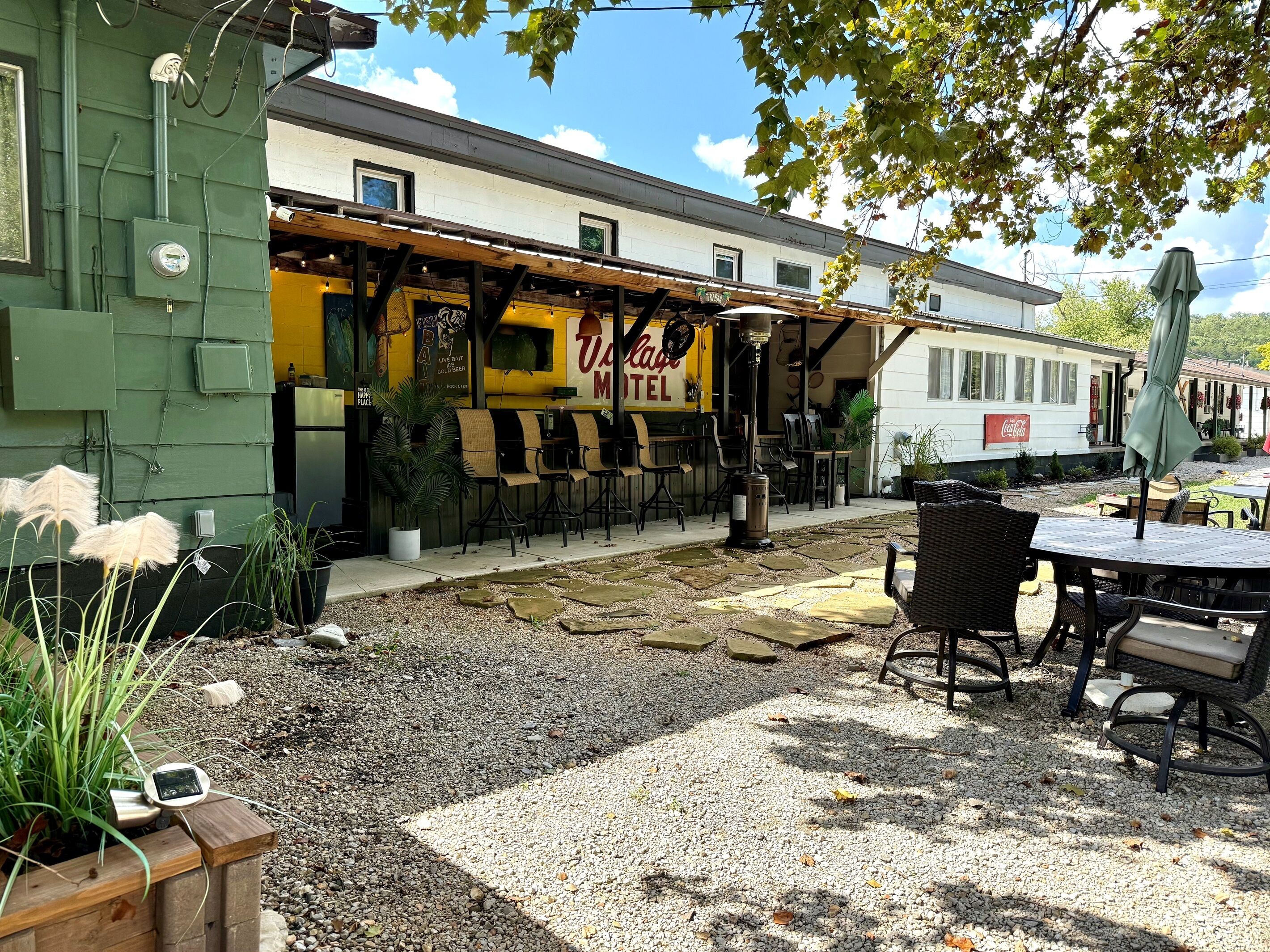 A patio area with outdoor seating, a building with a yellow awning, and a Coca-Cola sign.