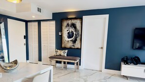 Un salon moderne avec un sol en marbre, un canapé blanc, une table à manger avec des chaises, une grande peinture abstraite et un téléviseur fixé au mur.