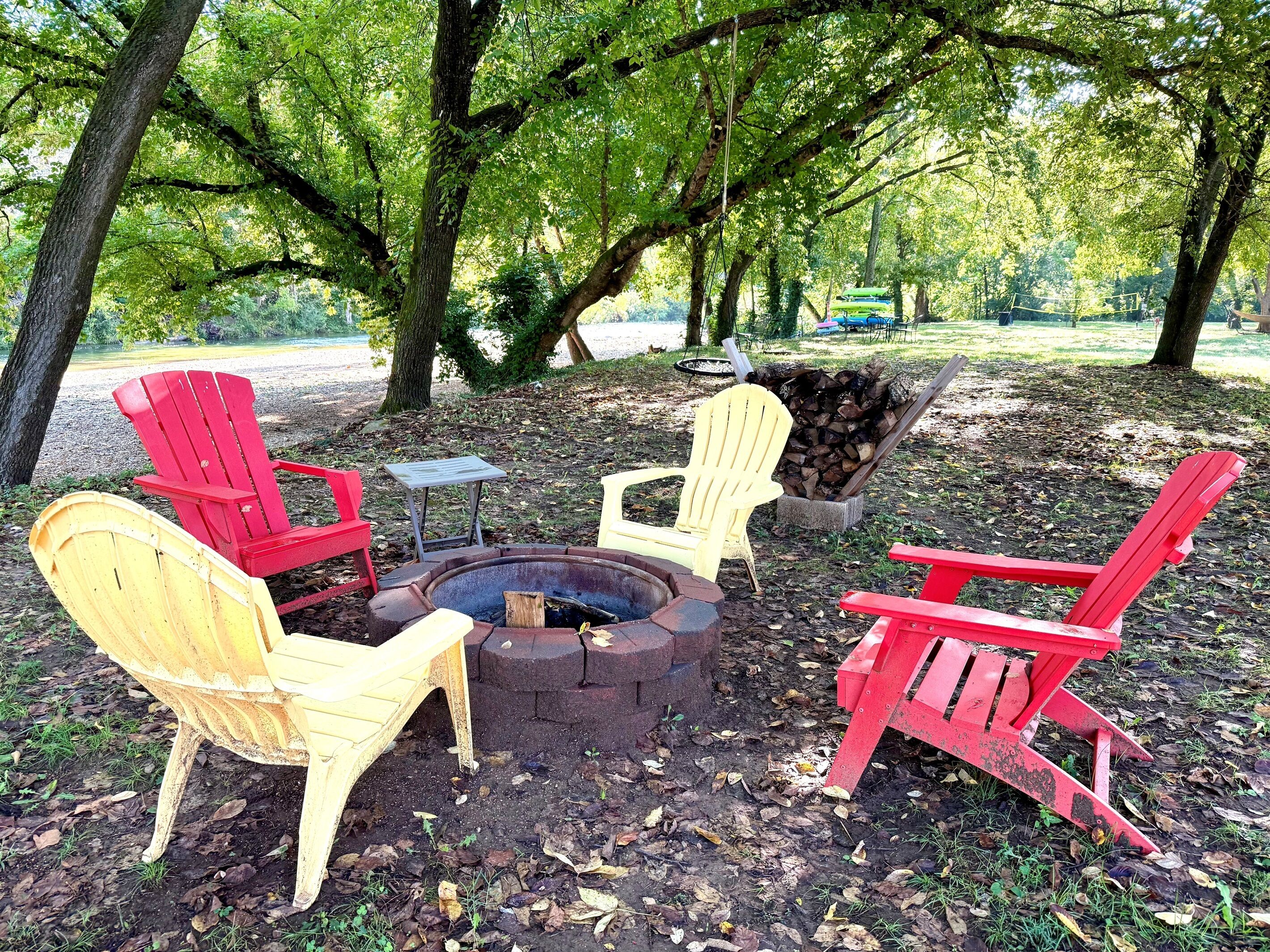 A fire pit surrounded by Adirondack chairs in a park setting.