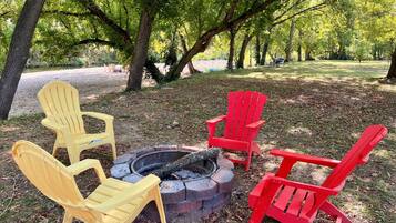 A fire pit with four Adirondack chairs, surrounded by trees in a park setting.