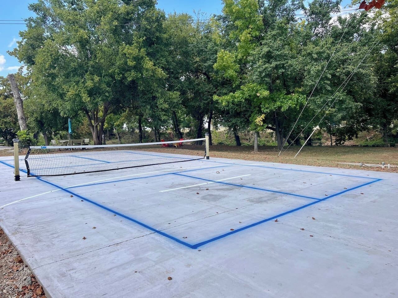 Ein Tennisplatz im Freien mit Netz, umgeben von Bäumen.