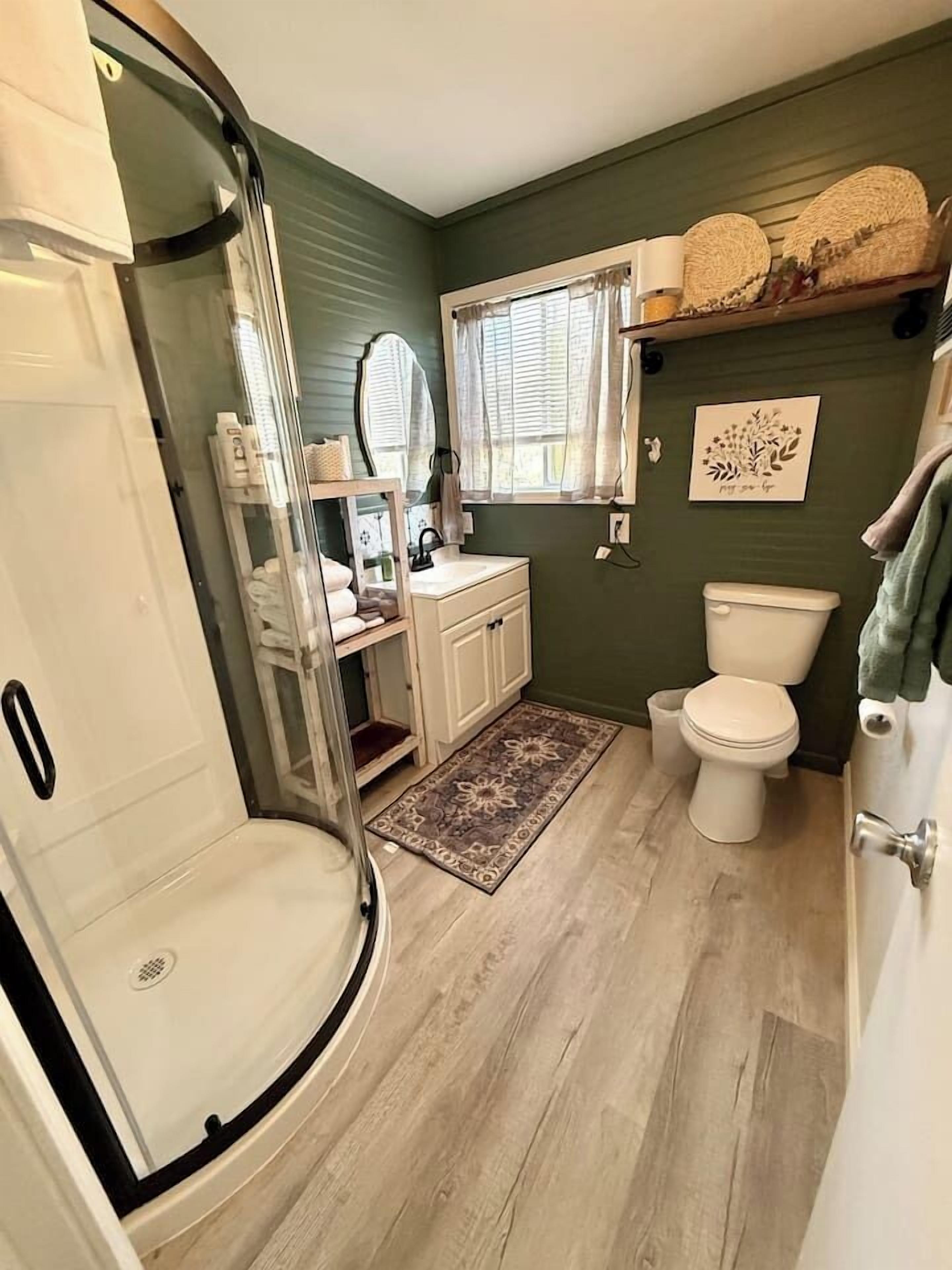 A bathroom with a shower, toilet, sink, and a mirror.