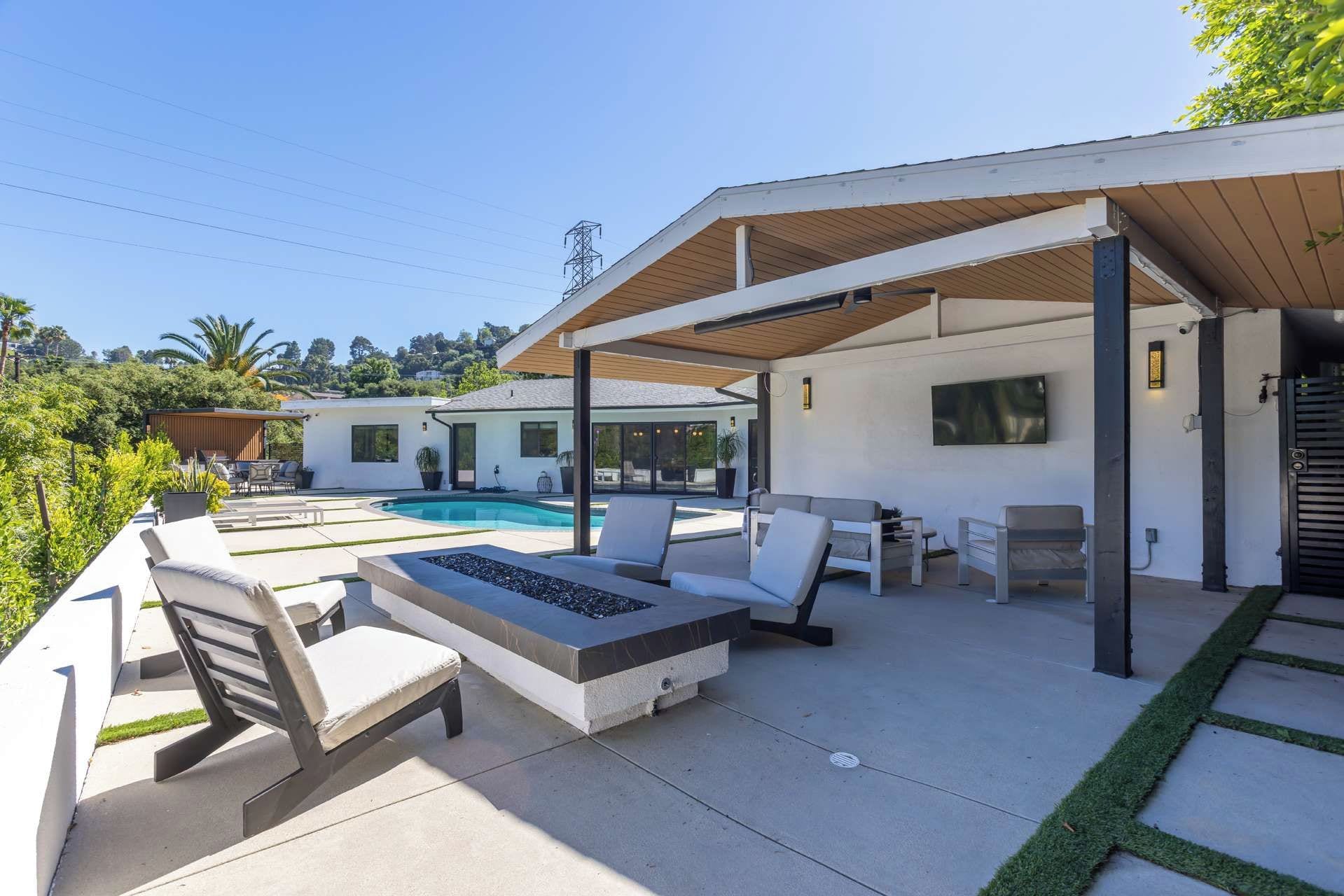 A modern outdoor patio with a pool, lounge chairs, and a covered seating area.