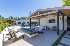 Un patio moderno al aire libre con piscina, sillas de descanso y una zona de estar cubierta.
