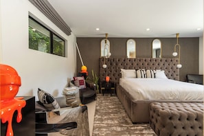 A modern bedroom with a tufted headboard, a large bed, bedside tables, a mirror, and a view of greenery outside. - Casa Dona by Oraklus (Beverly Hills)
