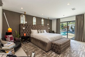 Ein modernes Schlafzimmer mit einem großen Bett, einer Sitzecke und Blick auf einen Swimmingpool.