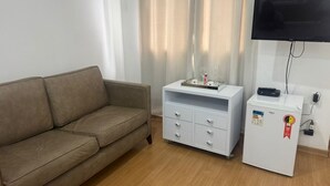 A room with a brown sofa, a white minibar with a flat-screen TV, and a small refrigerator. - Lindo Apto algumas quadras da Paulista (São Paulo)